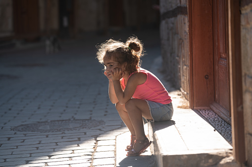 Portrait of 3,5 years old girl sitting on steps in entrance of house on the street. She is wearing a pink blouse. Shot with a full frame mirrorless camera under daylight.