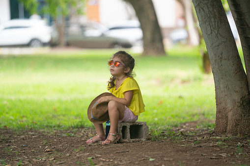 Rear photo of 3,5 years old girl wearing a yellow blouse sitting on green grasses in public park. Shot under daylight with a full frame mirrorless camera.