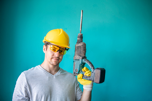Image of a Caucasian guy, a handyman with protective gear holding a drill in his hand.