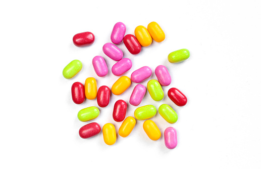 Small pill drops scattered on white surface. Pile of colorful bean shaped candies