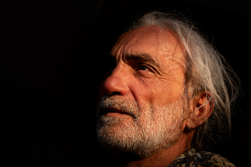 60 years old man black background looking away portrait white stubble.Sunset warm tones.