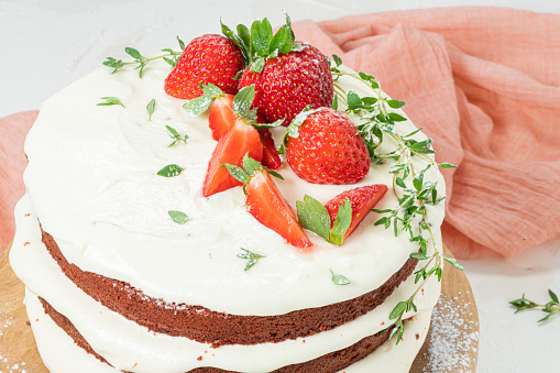 Stock photo showing close-up view of cake stand containing a cut, red velvet cake covered in butter cream and decorated with piped icing swirls dusted with dehydrated raspberry powder, displayed against a red background.