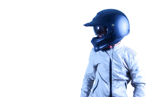 A young woman with long hair is smiling as she poses on her motorcycle, wearing a crash helmet and leather jacket. She enjoys an outdoor adventure surrounded by trees.
