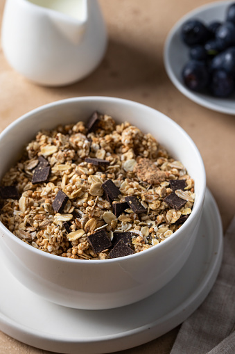 Granola with chocolate in white bowl served with blueberry and milk on the table. Healthy breakfast concept.
