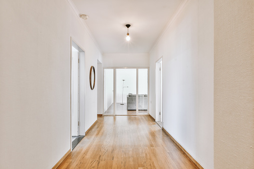 Perspective view of empty wide hallway with white walls and and parquet floor in minimalist style apartment