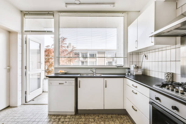 Corner cupboards and table located in light tiled kitchen of old flat with balcony