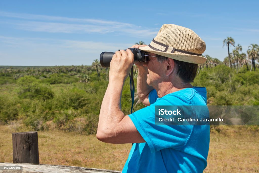 Latin senior man looking through binoculars, El Palmar National Park, Argentina Latin senior man looking through binoculars, visiting El Palmar National Park, in Entre Rios, Argentina, during his summer vacations. Travel and adventure, enjoyment of the outdoors, active retirement 70-79 Years Stock Photo