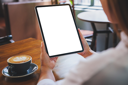 Mockup image of a woman holding digital tablet with blank white desktop screen in cafe