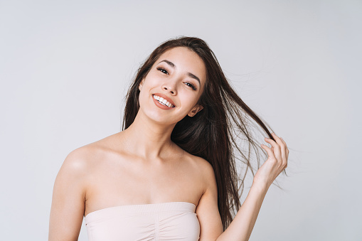 Beauty portrait of happy young beautiful asian woman with healthy dark long hair in top bando on white background isolated