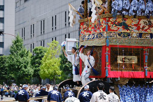 Kyoto, Japan - July 17, 2022: The naginata-boko, the lead float in the Gion Festival parade, has finished its second and final turn along the route. The two men riding in the front give the signal to pull the float forward with the attached ropes.