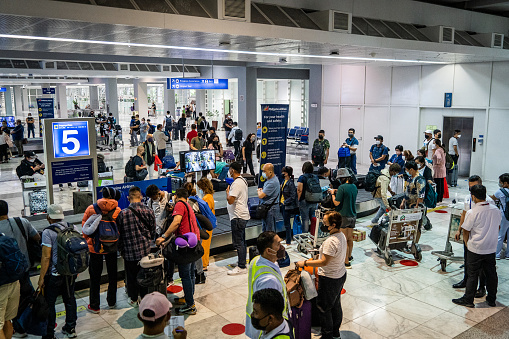 International travelers line up at baggage claim carousels at Manila Ninoy Aquino International Airport (MNL). International travel continues amid a worldwide surge in COVID infections from the highly contagious BA.5 variant, leading some countries to roll back pandemic-era travel requirements, including mask mandates and updated vaccine requirements to include booster shots for visa-free entry.