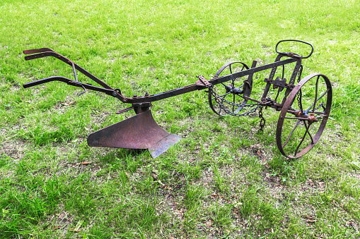 An old hand-made metal plow with wheels stands on the field. An ancient tool for plowing the soil