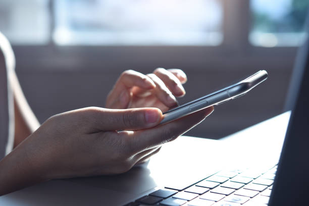 istock Business woman hand using mobile phone, finger touching on screen and working on laptop computer, close up 1409231572