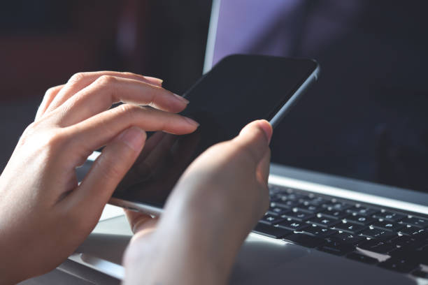 istock Business woman hand using mobile phone, finger touching on screen and working on laptop computer, close up 1409232205