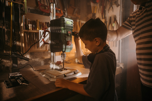 Grandfather teaching grandson to use bench drill in his small workshop
