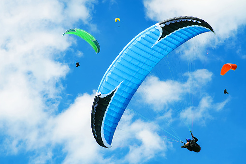 Yellow and orange paragliding on a blue sky with clouds on background