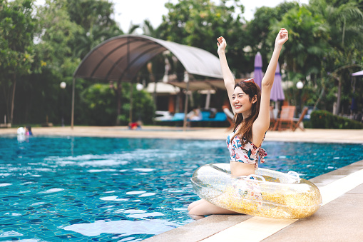 Southeast asia holidays summer travel concept. Happy smile raised hand young adult asian woman at hotel swimming pool.  People with satisfaction life moment at nature outdoor.