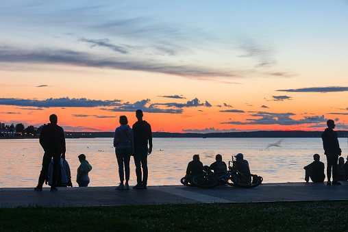 Unidentified silhouettes of people on the embankment of the city of Petrozavodsk in Karelia look at the evening colorful sky after sunset.