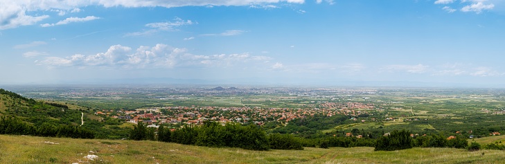 Panorama on ancient intermountain town Plovdiv with old residential houses and farm green fields, against backdrop of Rhodope Mountains and hills covered with evergreen spruce forests and cloudy sky