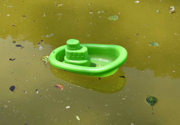 Green toy plastic boat in small pond with green water and plant debris. Pond of the laundry of the village of Armejún, province of Soria, Spain. toy boat stock pictures, royalty-free photos & images