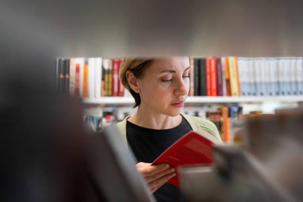 istock Female Mature Student Looking For Book At Library Bookshelf Studying At University Campus Or College 1409253050