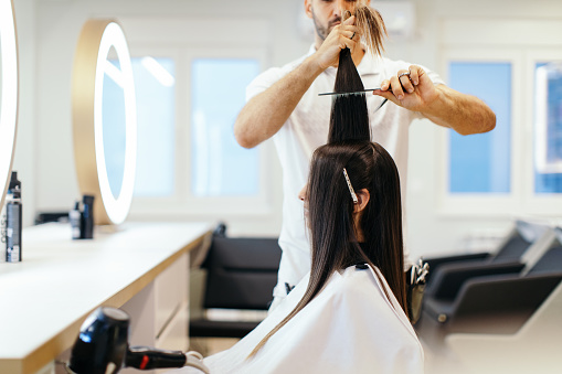 Young beautiful woman is in hair salon. Hairdresser is combing her hair