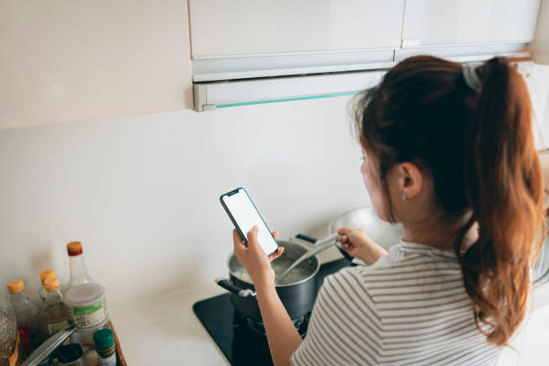 istock Young Asian Woman Preparing Breakfast and Using Mobile Phone in Domestic Kitchen 1409263813