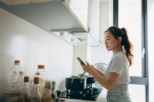istock Young Asian Woman Preparing Breakfast and Using Mobile Phone in Domestic Kitchen 1409263818