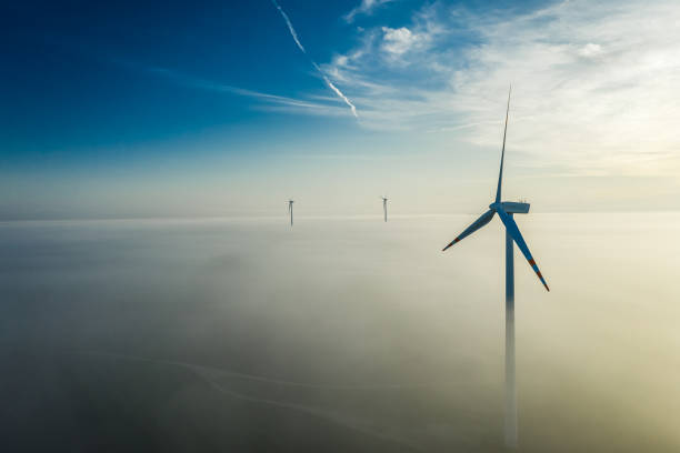 Misty sunrise and wind turbine with sun rays stock photo