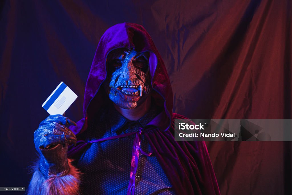 Monster with a credit card Portrait of a zombie dressed in a shirt and hooded cape holding a credit card as seen from the magnetic stripe side. The scene is dark, illuminated by blue and orange lights. Credit Card Stock Photo