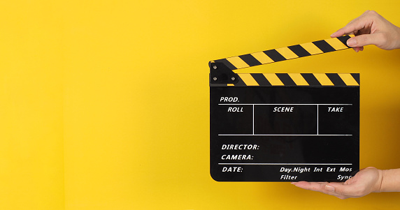 The man's hands are holding black with yellow clapper board or movie slate on yellow background.