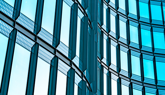 Glass and steel facade of a modern high rise office building with illuminated windows, view on empty rooftops. Conceptual background for construction industry, financial district, corporate business. Digitally generated image.
