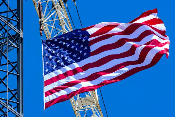 A construction site crane flying a United States Flag with a clear blue sky on a bright sunny day