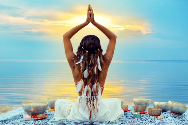 yoga meditation at sunset beach. peaceful woman relaxing with tibetan singing bowls. indian women silhouette meditating over sunshine blue sky background - sea zen like landscape water imagens e fotografias de stock