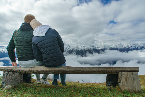 Romantic couple of man and woman on in mountain sitting on bench look of mountains observing view