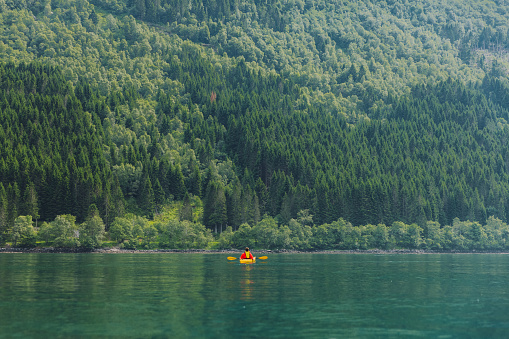 Male explorer sitting in the yellow kayak paddling on the fjord with a view of the beautiful mountains