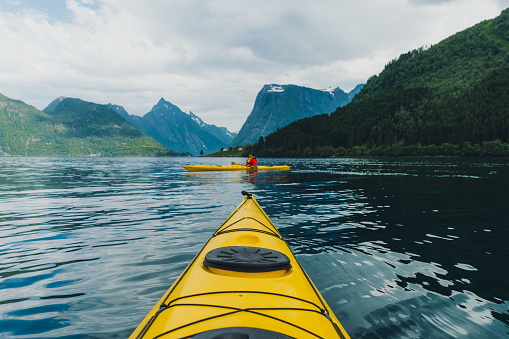 Woman and man explorers paddling on a yellow kayak on the fjord with a view of the beautiful mountains in Norway