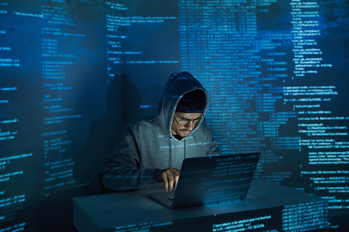 Confident young man in hooded shirt using computer against dark background