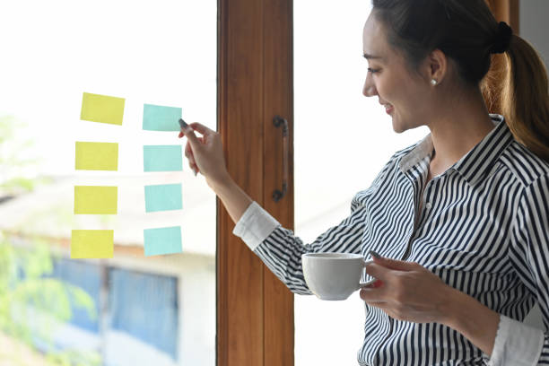 istock Side view of an Indian Asian female looking thoughtful at a paper note on the window while holding a cup of coffee. Business and financial concepts. 1409294973