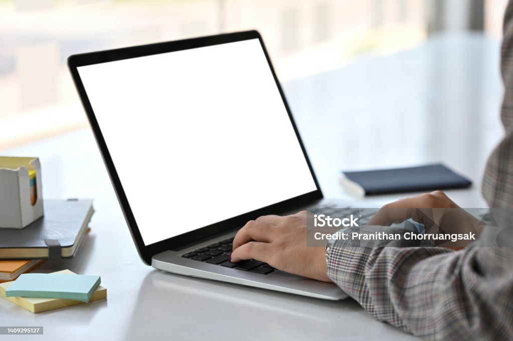 Close up side view of an adult female in a suit typing something with an empty monitor screen of a laptop on a busy white desk. Business and Technology concepts. Computer Monitor Stock Photo