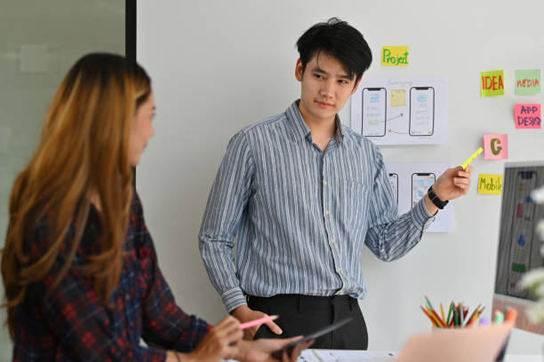 istock Thai young adult male pointing data on the whiteboard presenting projects to co-workers in the modern office interior. Technology and design concepts. 1409295928