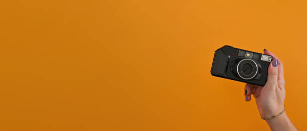 istock Front view close up with a right male hand holding a digital camera model with his color nails and a bangle over an orange background. 1409296184