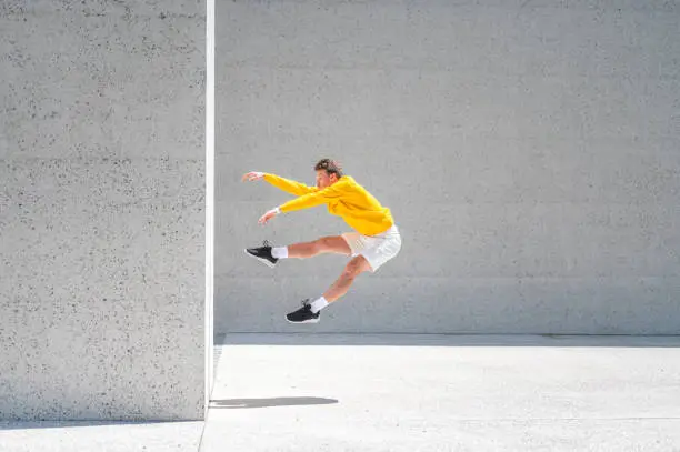 Photo of Young man jumping by the big concrete wall outdoors