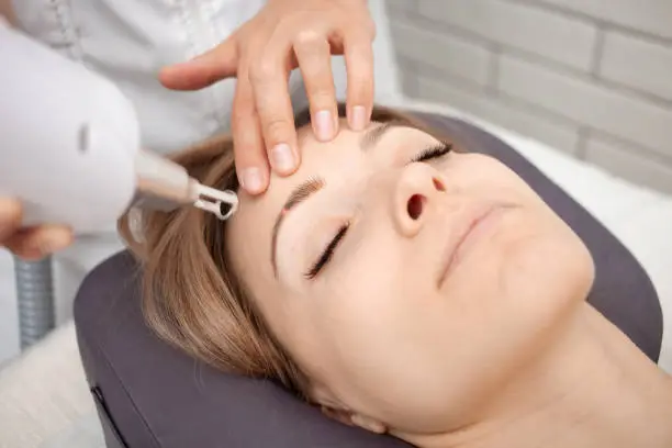 Photo of cosmetologist removes permanent makeup, eyebrow tattooing with laser.