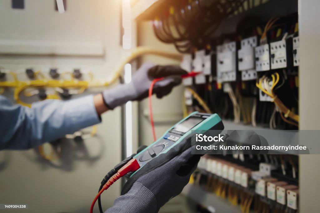 Electricity and electrical maintenance service, Engineer hand holding AC multimeter checking electric current voltage at circuit breaker terminal and cable wiring main power distribution board. Electrician Stock Photo