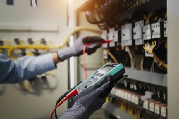 Photo of Electricity and electrical maintenance service, Engineer hand holding AC multimeter checking electric current voltage at circuit breaker terminal and cable wiring main power distribution board.