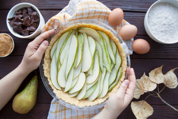 istock Female hand holds fall pear pie on brown table. Autumn leaves decor and ingredients. 1409306990