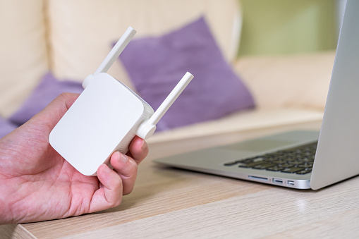 Selective focus at range extender. Internet router on working table with blurred man connect the cable at the background. Fast and high speed internet connection to cover home network usage.
