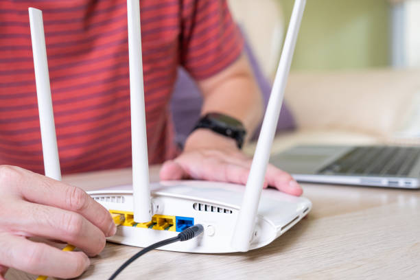 istock Selective focus at router. Internet router on working table with blurred man connect the cable at the background. Fast and high speed internet connection from fiber line with LAN cable connection. 1409308635