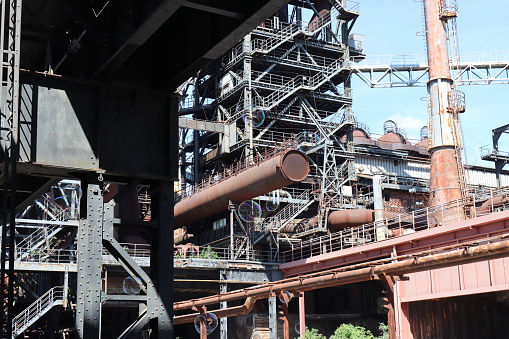 Historic Steelstacks, an abandoned steel factory in Bethlehem, Pennsylvania, featuring a long walkway leading towards massive old rusted structures, set against a clear sky. The empty tracks and aged buildings reflect the industrial past and resonate with themes of industrial decline and historical preservation.